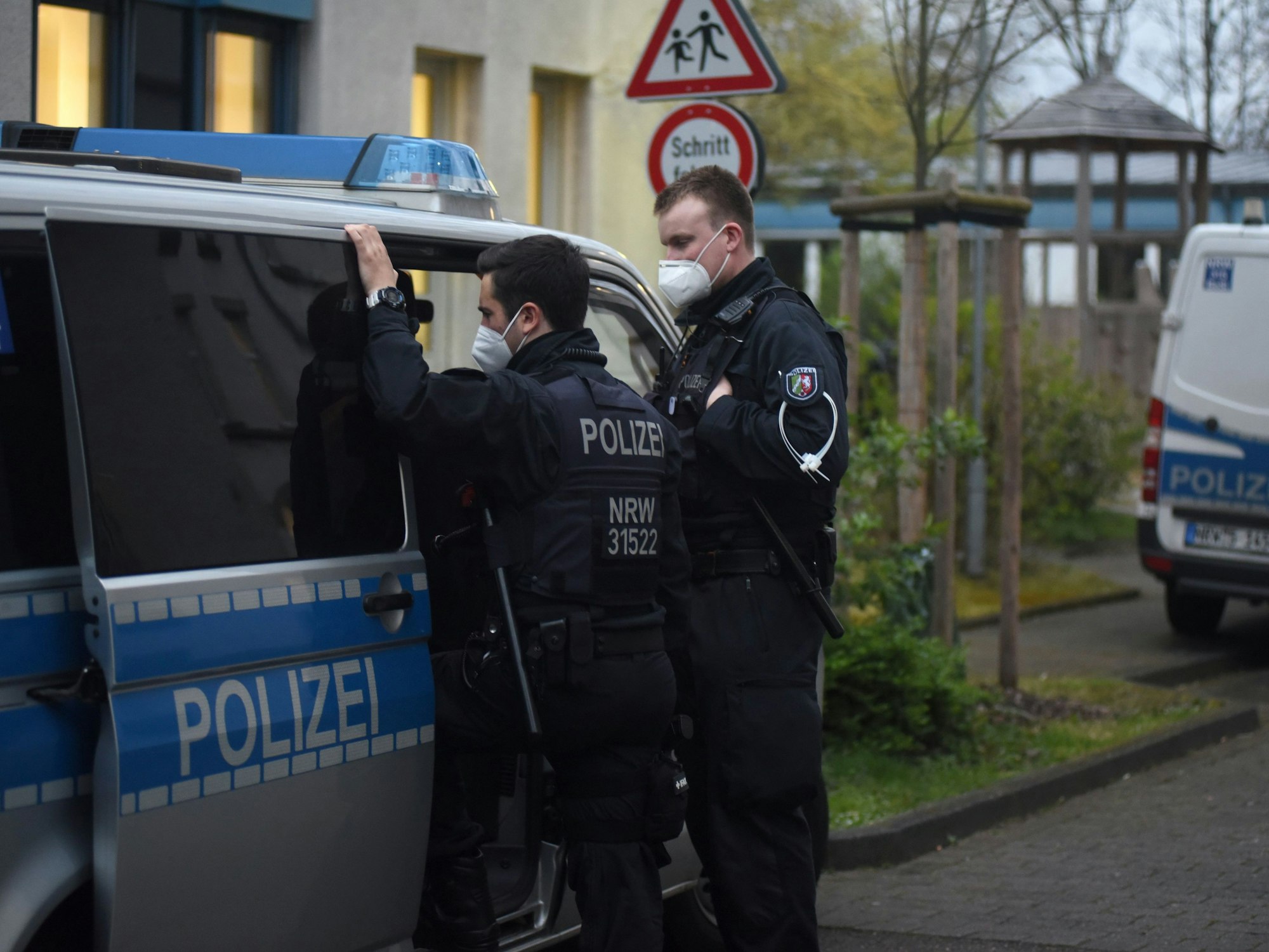 Zwei Polizisten stehen bei einer Razzia an einem Streifenwagen.