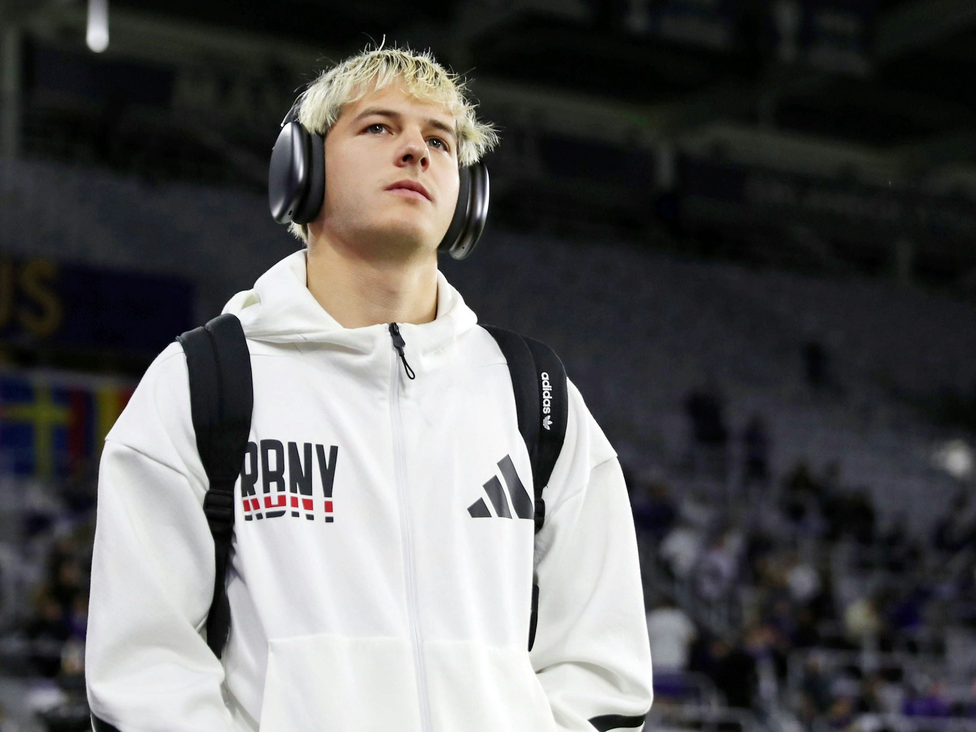 John Tolkin kommt mit Trainingsjacke und Kopfhörern ins Stadion.