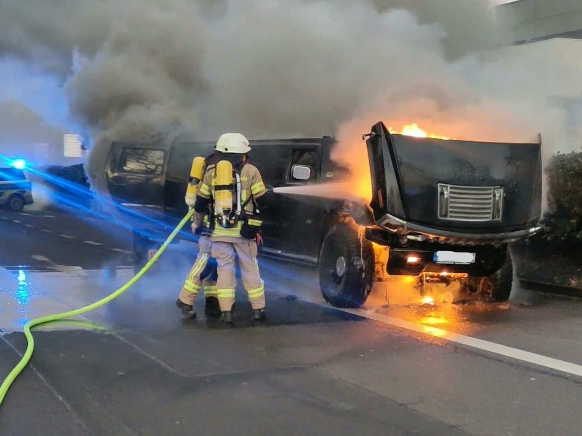Feuerwehr steht an einem brennenden Auto, im Hintergrund steigt dichter Rauch auf.