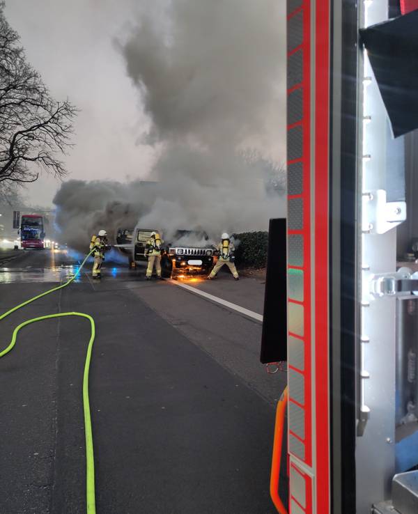 Brennendes Auto auf einer Straße in Köln, die Feuerwehr löscht.