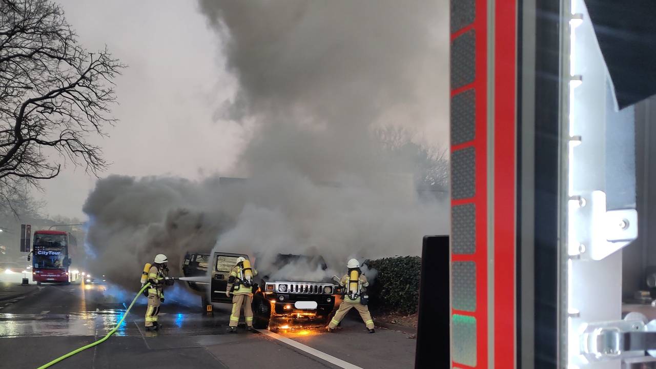 Brennendes Auto auf einer Straße in Köln, die Feuerwehr löscht.