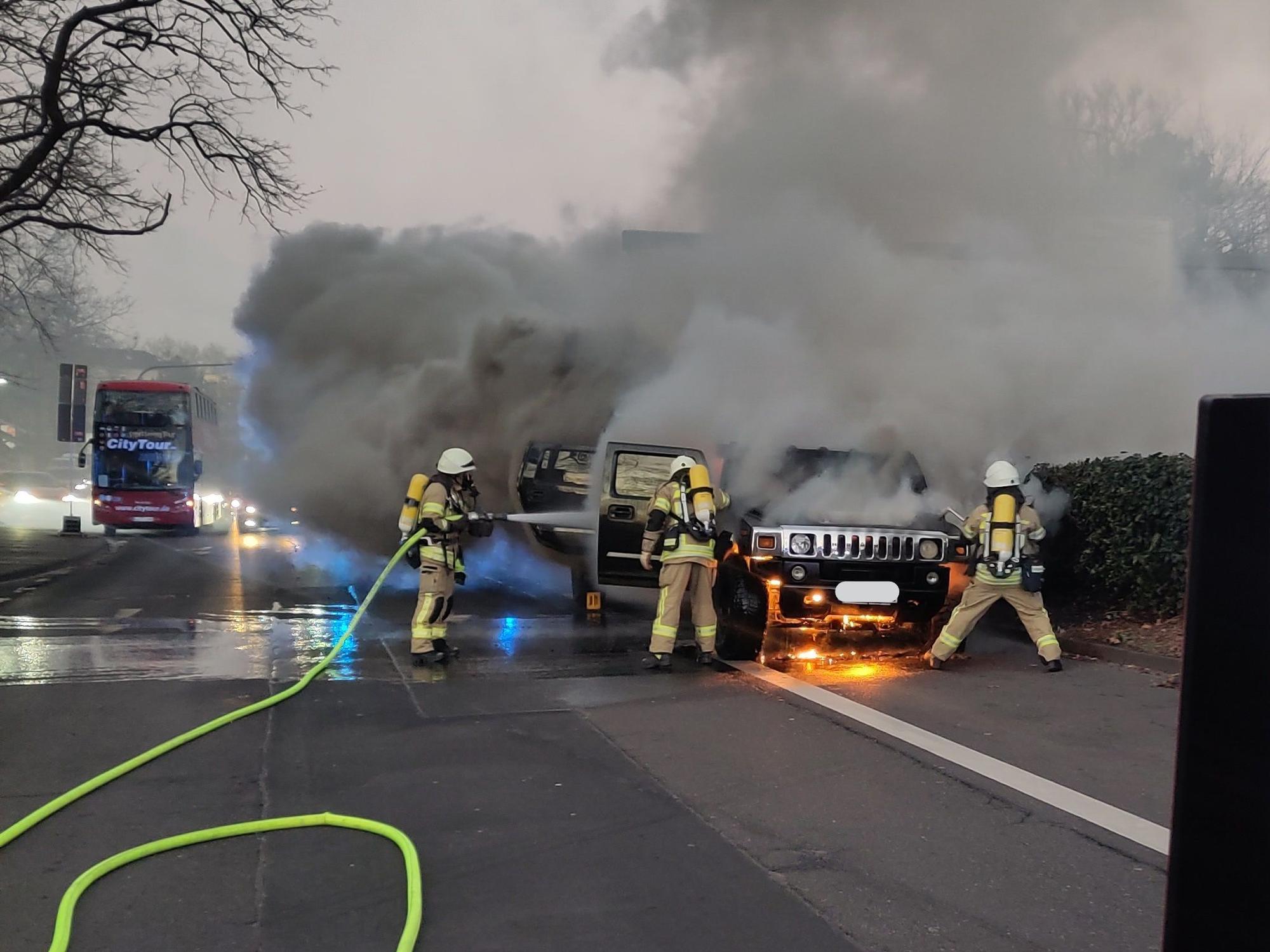 Brennendes Auto auf einer Straße in Köln, die Feuerwehr löscht.