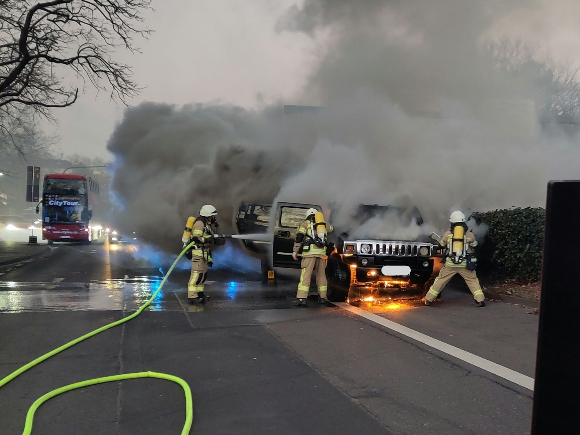 Brennendes Auto auf einer Straße in Köln, die Feuerwehr löscht.