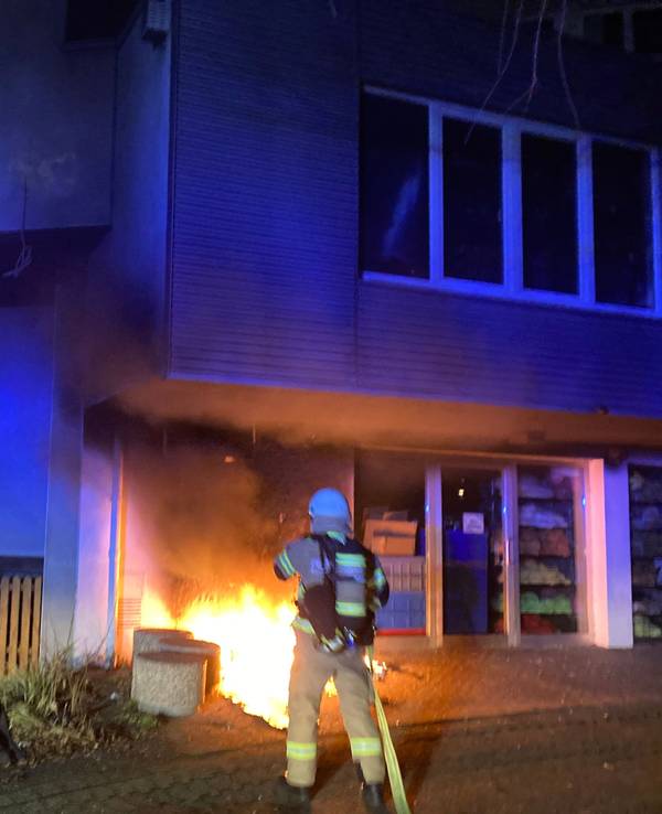 Ein Feuerwehrmann hält mit dem Löschschlauch auf einen Brand direkt an einem Gebäude.
