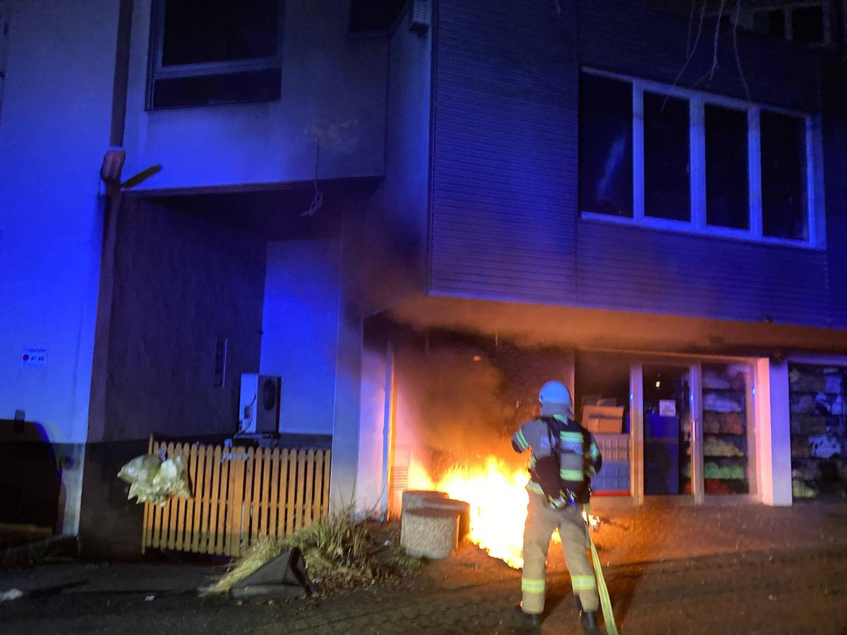 Ein Feuerwehrmann hält mit dem Löschschlauch auf einen Brand direkt an einem Gebäude.