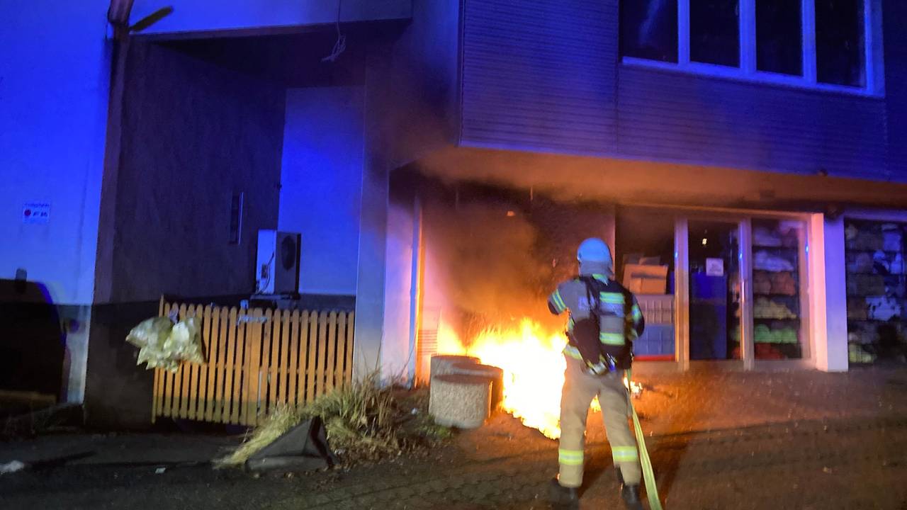 Ein Feuerwehrmann hält mit dem Löschschlauch auf einen Brand direkt an einem Gebäude.