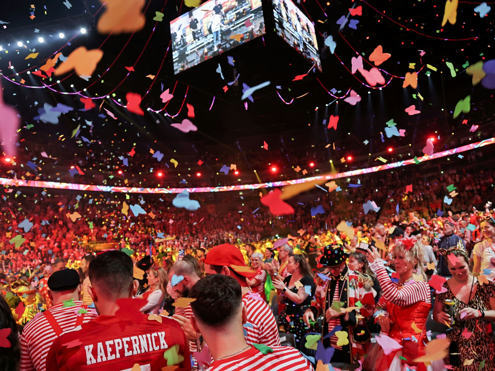 Jecke stehen in der Lanxess-Arena im Konfettiregen.