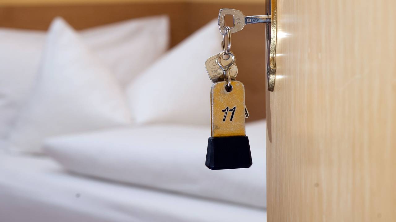 Ein Zimmerschlüssel hängt in einem Gästehaus vor einem Bett im Türschloss. (Symbolfoto)
