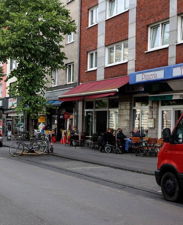 Autos auf der Venloer Straße in Köln, an den Straßenrändern sind Cafés und andere Außengastro zu sehen.
