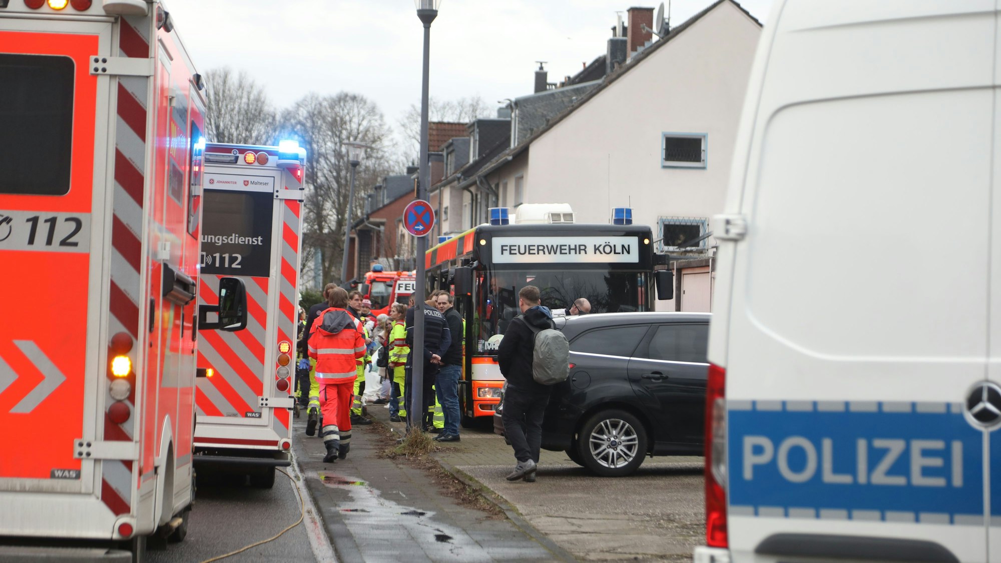 Einsatzfahrzeuge von Polizei, Rettungsdienst und ein Bus der Kölner Feuerwehr sowie zahlreiche Einsatzkräfte stehen an und auf einer Straße.