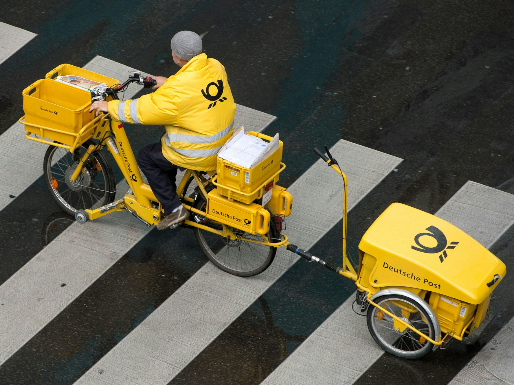 Ein Briefträger der Deutschen Post fährt mit einem Fahrrad (E-Bike) über einen Zebrastreifen in Stuttgart (Archivbild). Auch am Mittwoch dürften viele Menschen vergeblich auf Briefe und Pakete warten.