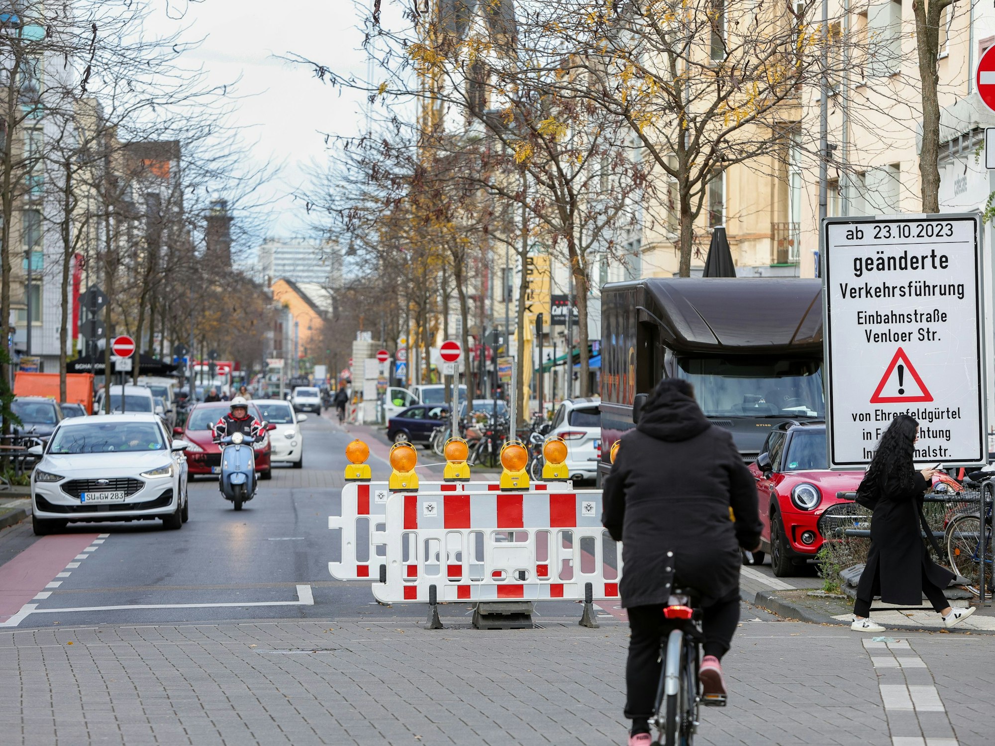 Eine Fahrbahnrichtung einer Straße ist mit Warnbaken gesperrt, ein Schild weist auf eine geänderte Verkehrsführung hin.