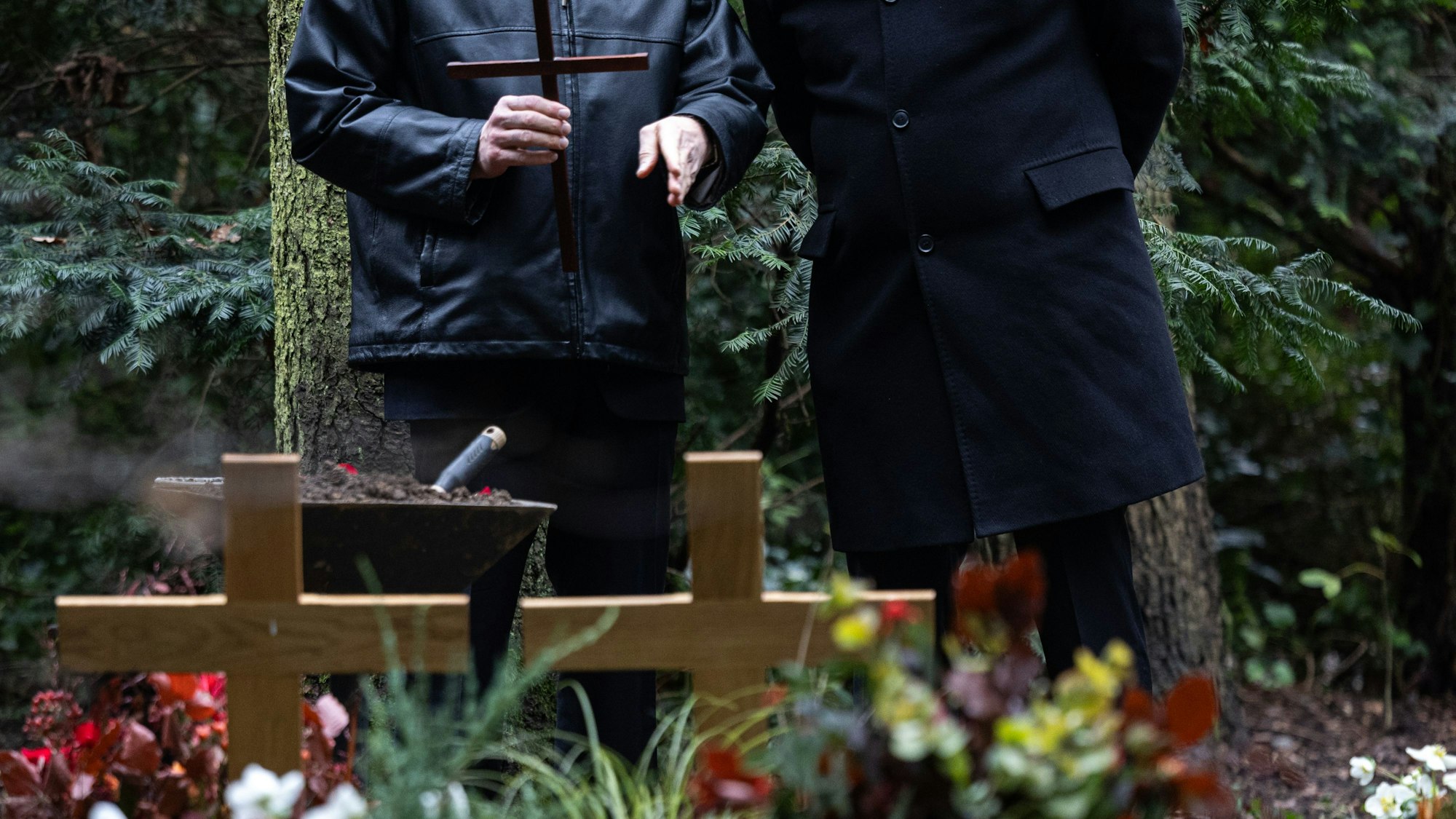 Zwei Menschen stehen vor einem Grab mit Holzkreuzen (Symbolfoto vom 6. Dezember 2024). Nach dem Sturz einer Seniorin auf dem Friedhof in Bensberg hat nun das Kölner Landgericht entschieden.