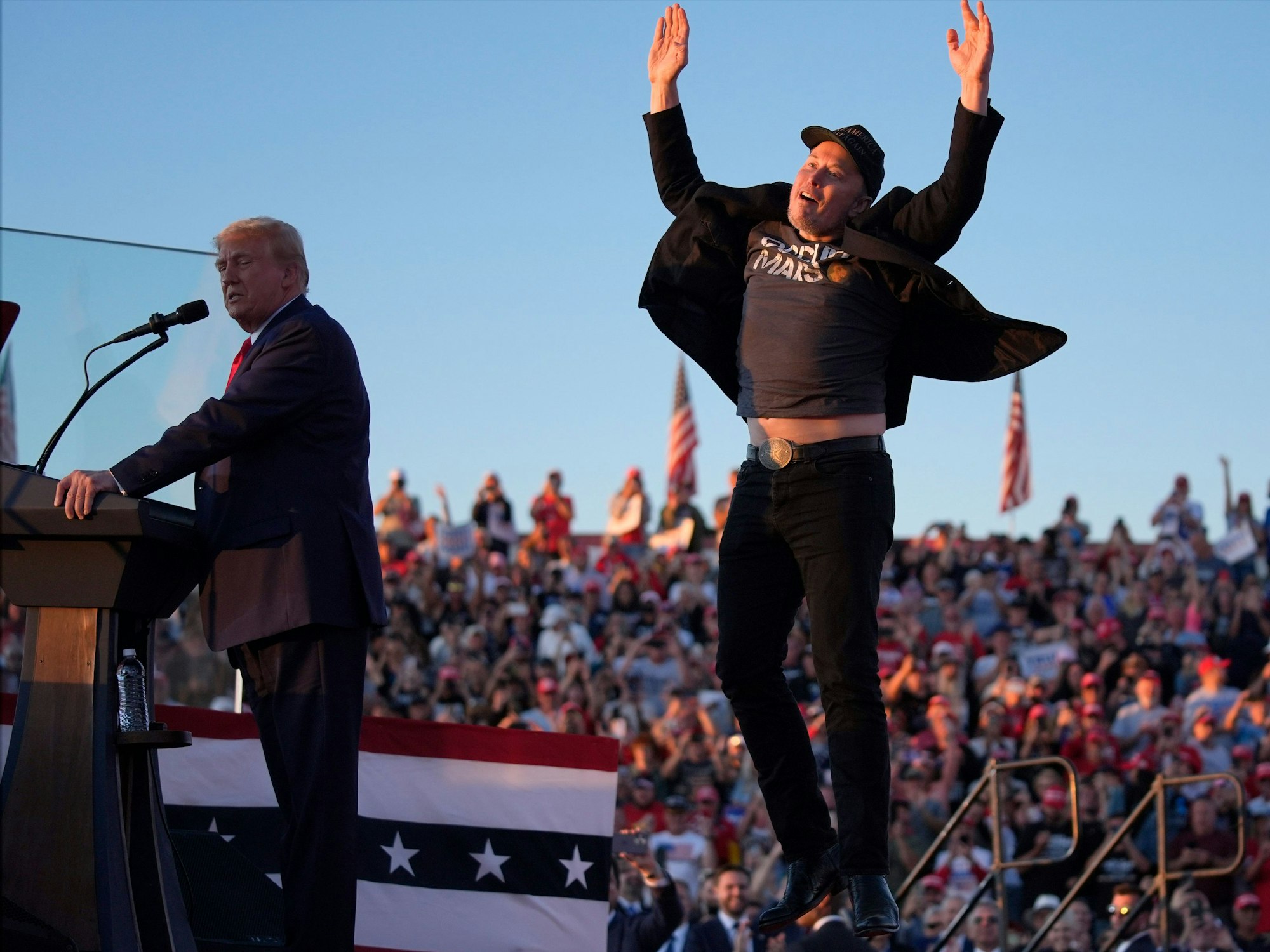 Elon Musk springt auf der Bühne, während der republikanische Präsidentschaftskandidat und ehemalige US-Präsident Donald Trump bei einer Wahlkampfveranstaltung bei der Butler Farm Show spricht.