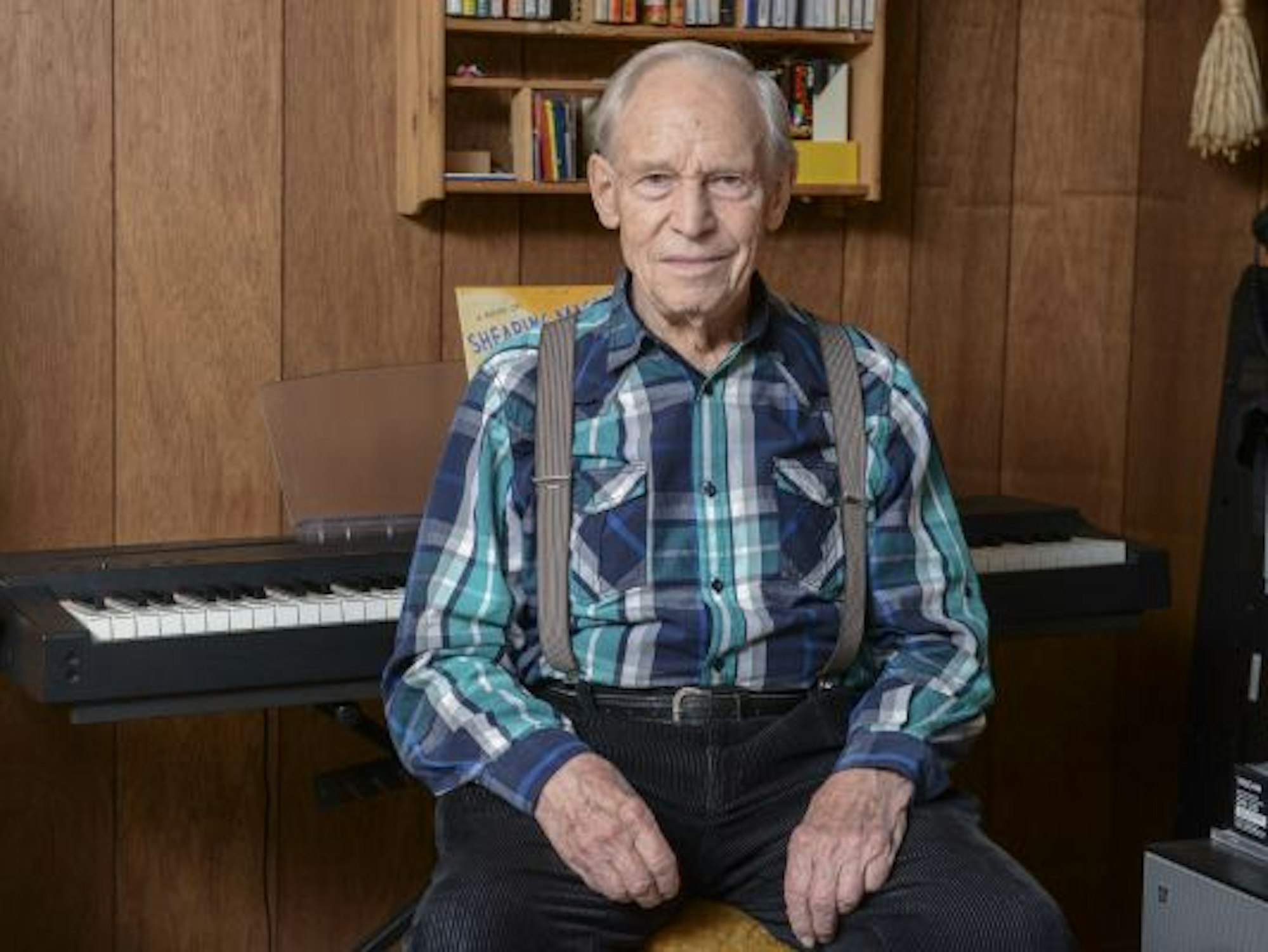 Ein älterer Mann sitzt auf einem Hocker vor einem Keyboard.