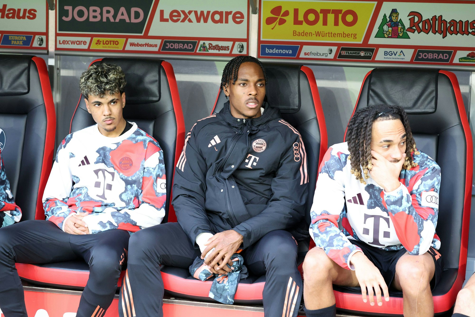 Adam Aznou (l.), Mathys Tel (M.) und Sacha Boey auf der Ersatzbank des FC Bayern.