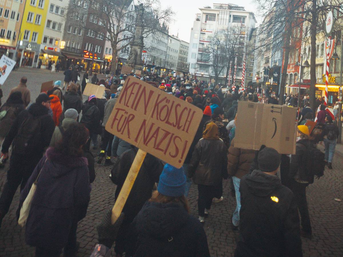 Eine Person hält in einer Menschenmasse ein Schild mit der Aufschrift „Kein Kölsch für Nazis“ hoch.