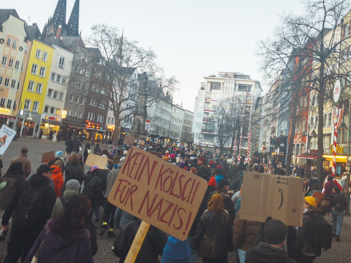 Eine Person hält in einer Menschenmasse ein Schild mit der Aufschrift „Kein Kölsch für Nazis“ hoch.