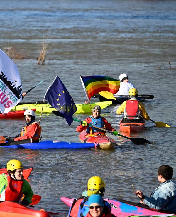 Menschen in Kanus sind auf dem Wasser und halten Fahnen mit der Aufschrift „Kein Rassismus“.