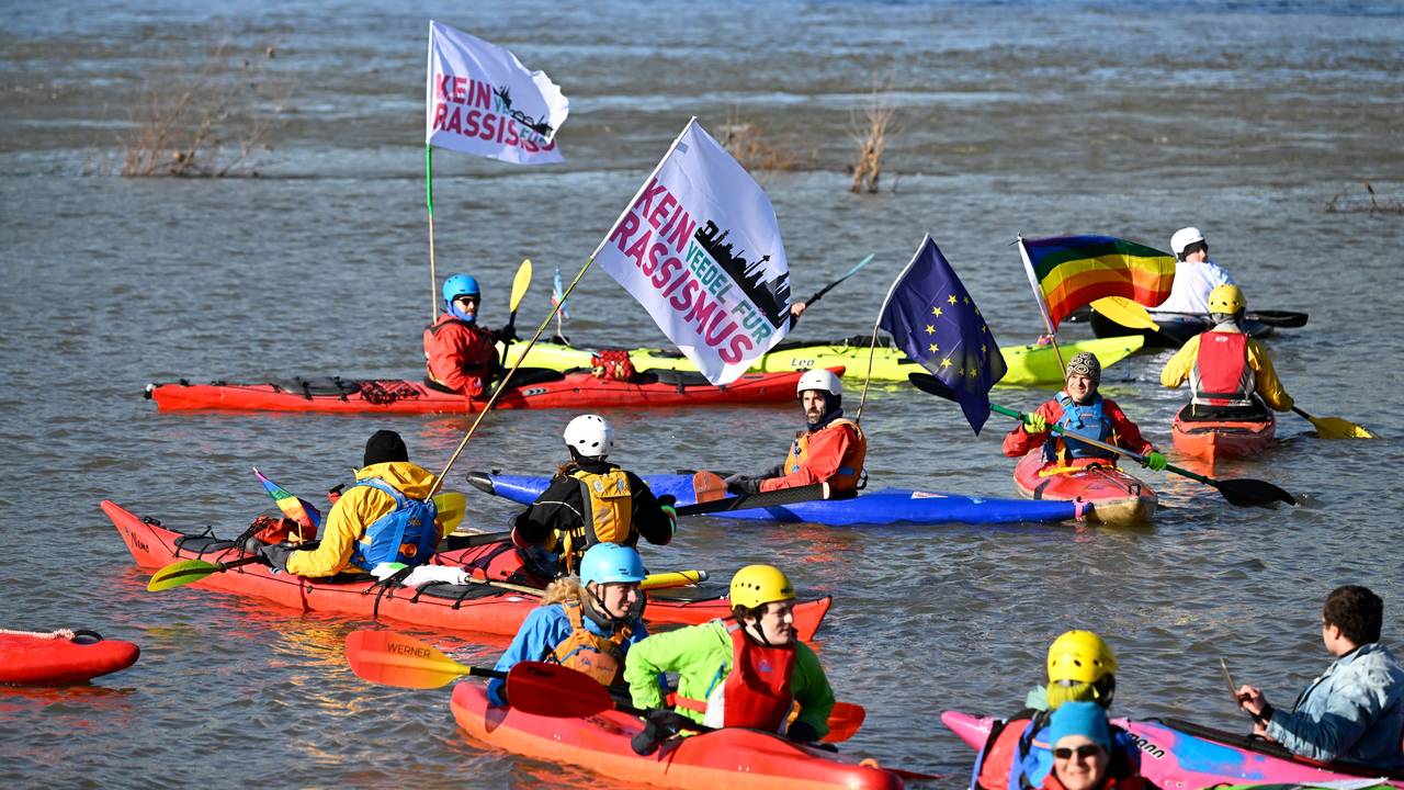 Menschen in Kanus sind auf dem Wasser und halten Fahnen mit der Aufschrift „Kein Rassismus“.
