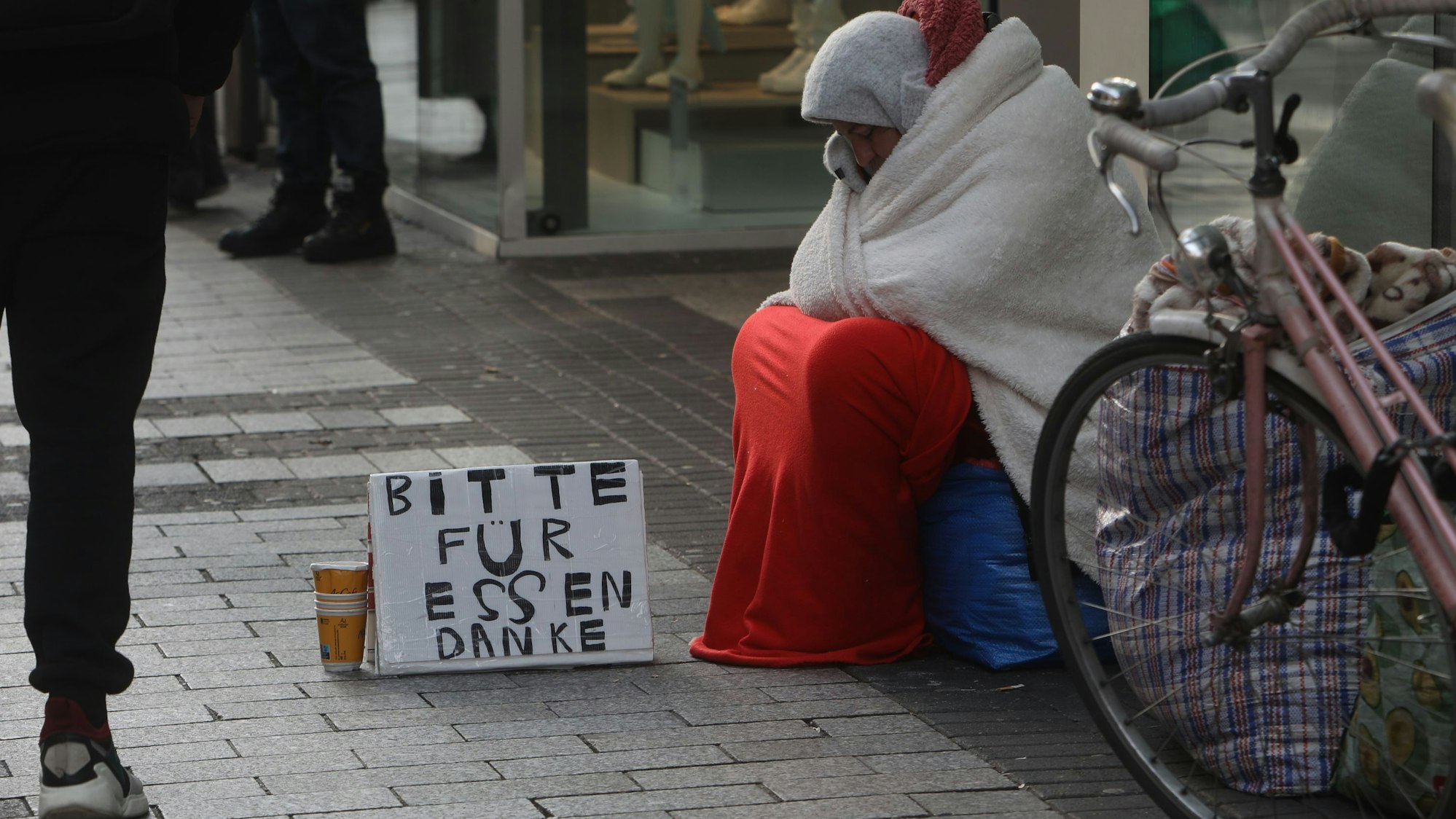 Eine Bettlerin sitzt mit einem Schild an einem Straßenrand.