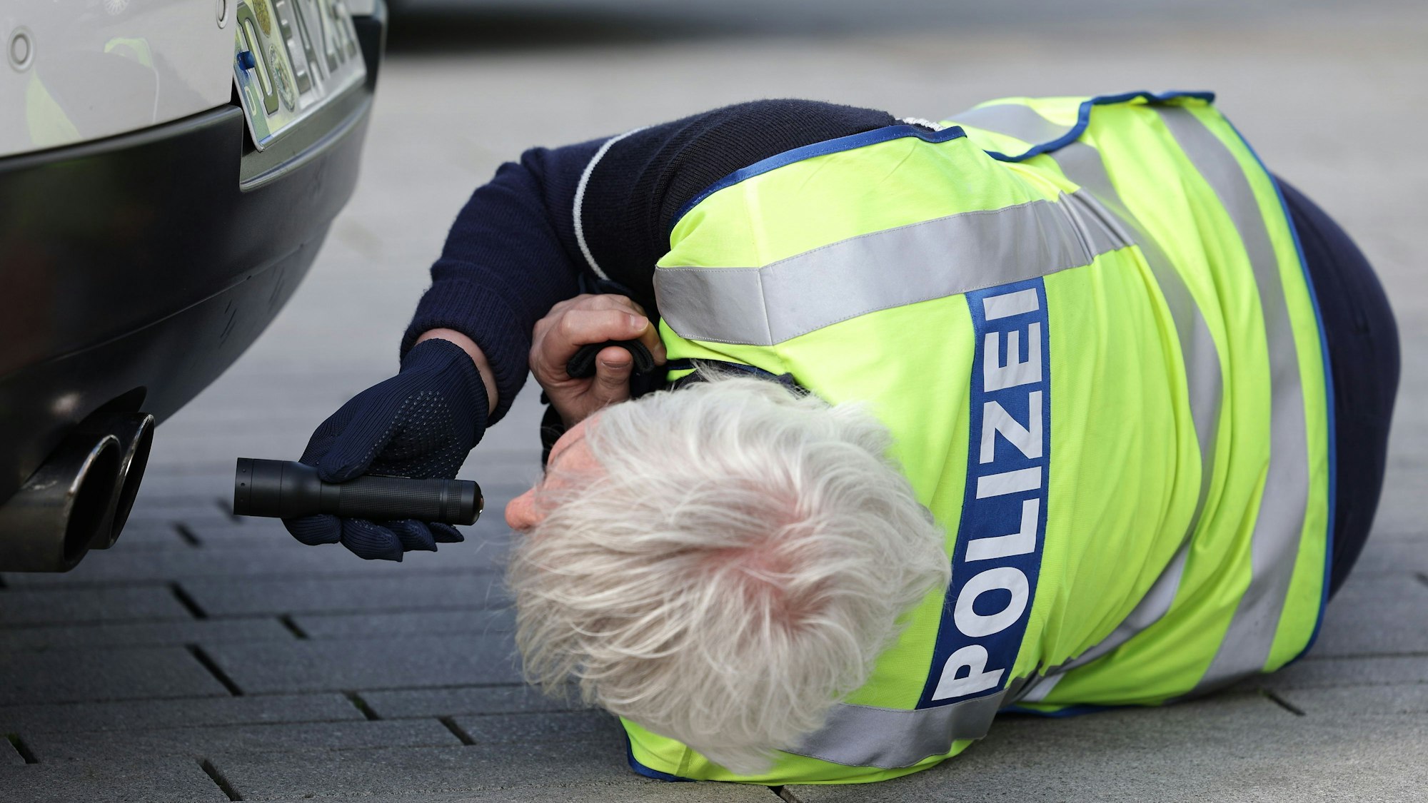 Ein Polizist leuchtet beim Tuner- und Poser-Treffen am "Car-Freitag" mit einer Taschenlampe in den Auspuff eines Fahrzeuges.