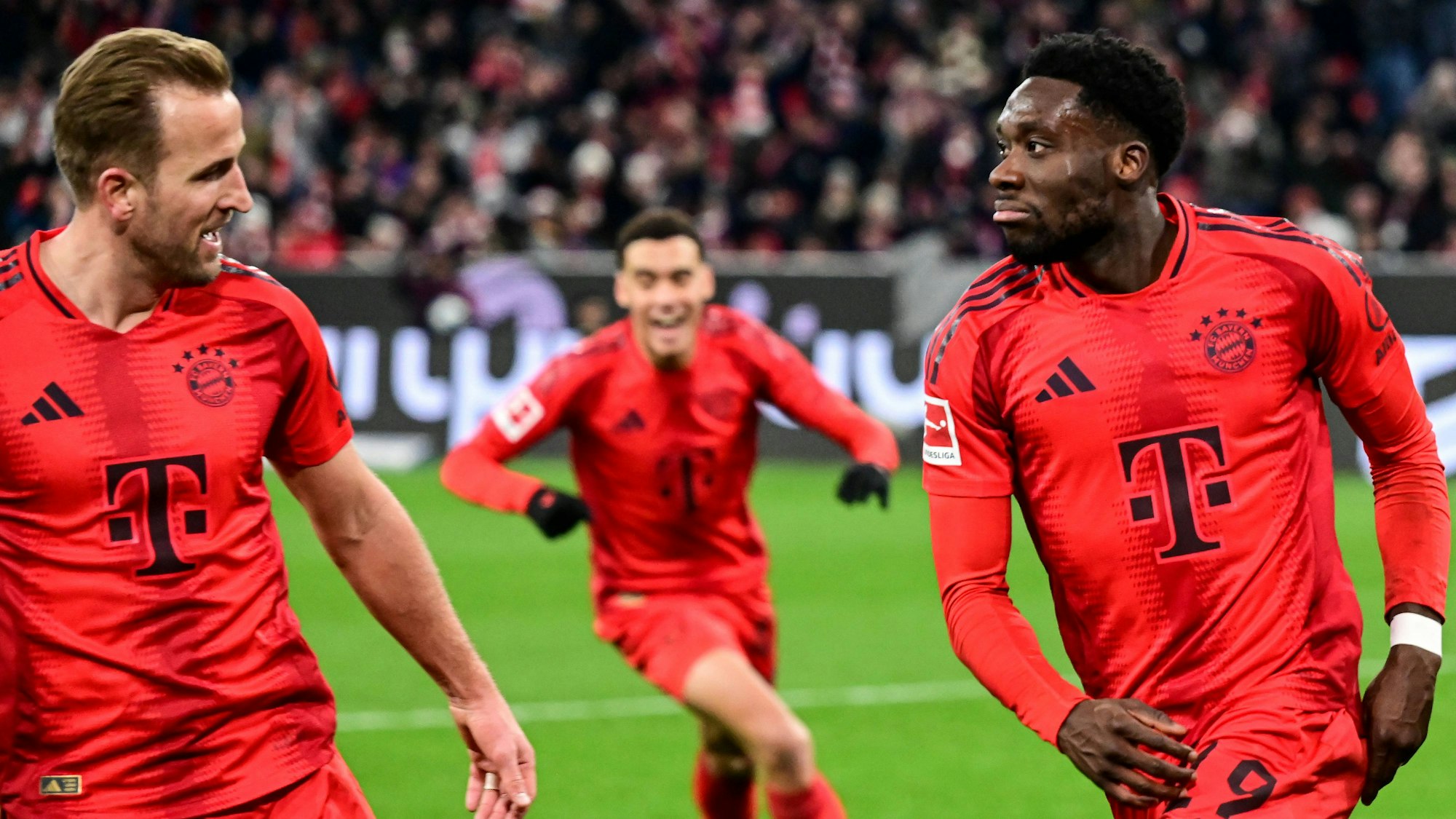 Harry Kane, Jamal Musiala und Alphonso Davies jubeln gemeinsam im Trikot des FC Bayern.