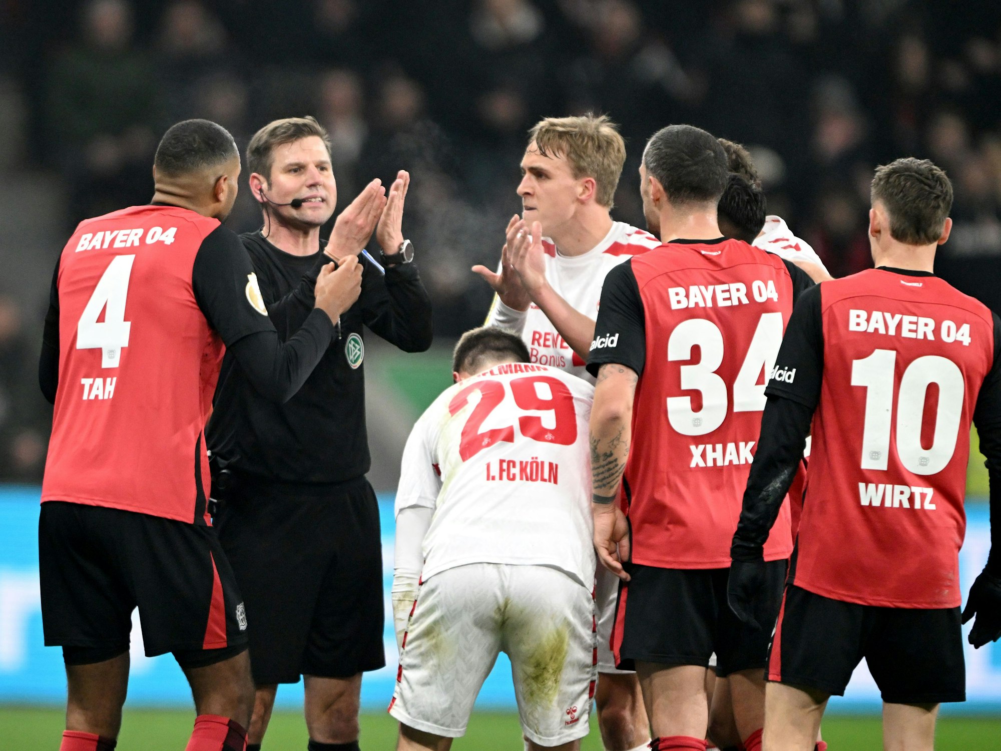 Die Spieler von Bayer Leverkusen und dem 1. FC Köln diskutieren mit Schiedsrichter Frank Willenborg.