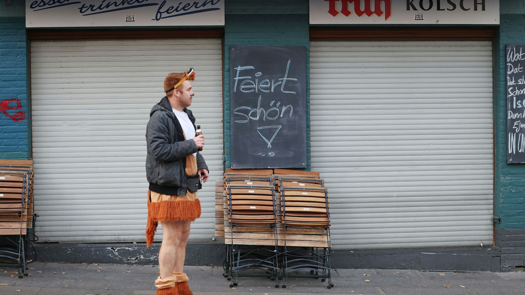 Ein Karnevalist steht 2021 vor einer geschlossenen Kneipe in Köln, an der ein Schild mit der Aufschrift „Feiert schön!“ hängt. Die Zahl der Kneipen in NRW ist deutlich gesunken.
