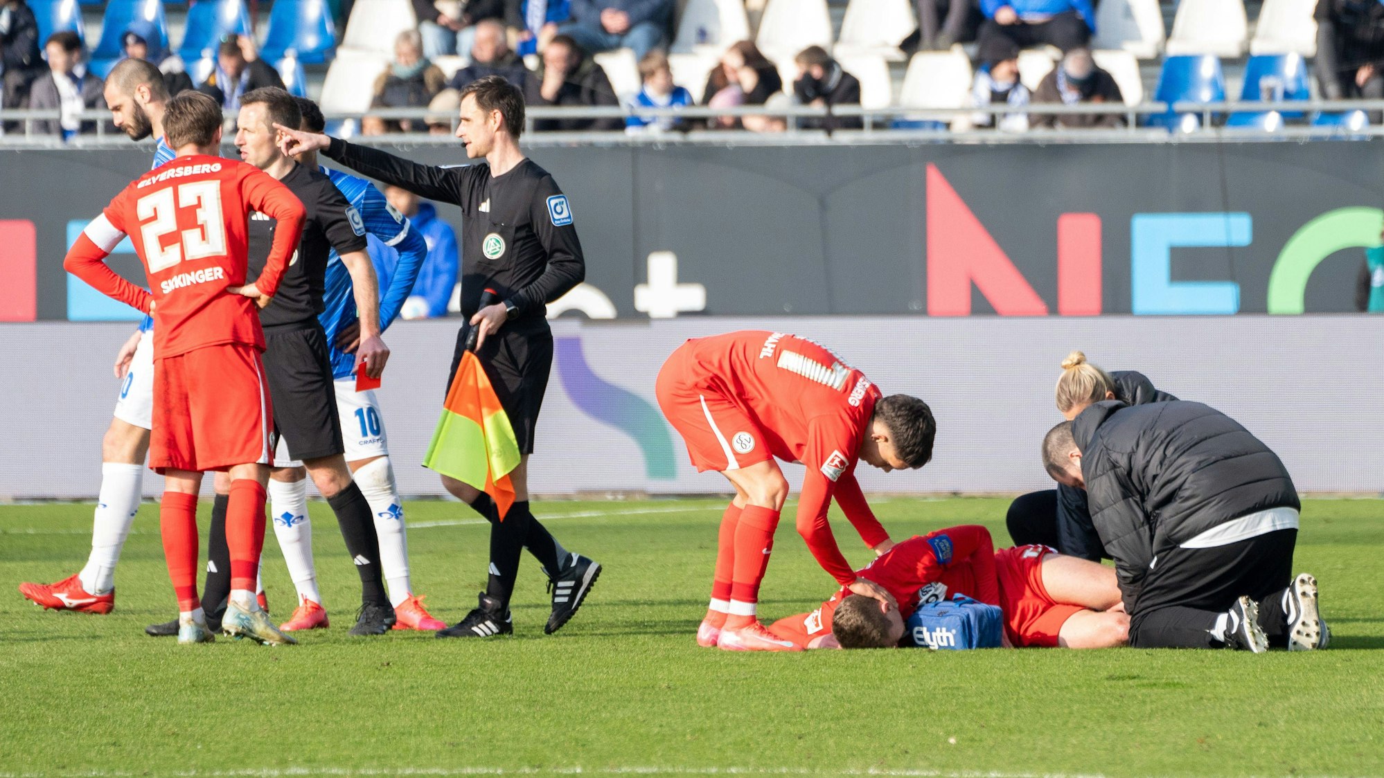 Während der verletzte Elias Baum (SV Elversberg) behandelt wird, beraten sich Schiedsrichter Lukas Benen und sein Assistent über die Konsequenzen des Ausrasters von Darmstadt-Profi Fabian Nürnberger.