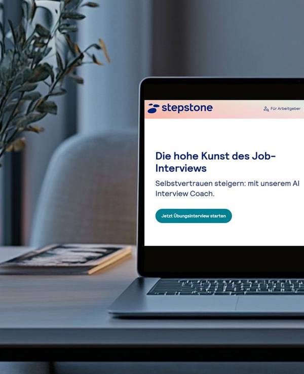 Ein Laptop steht geöffnet auf einem Schreibtisch. Das Display zeigt die Website von StepStone und die Seite des AI Interview Coach.