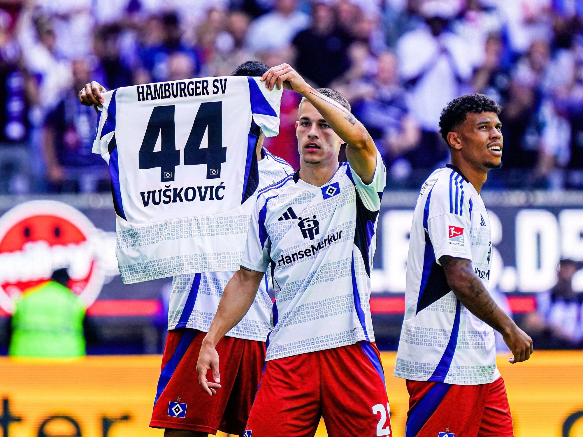 Die HSV-Profis Miro Muheim (r.) und Robert Glatzel halten das Trikot ihres gesperrten Team-Kollegen Mario Vuskovic in die Höhe. (31. August 2024)