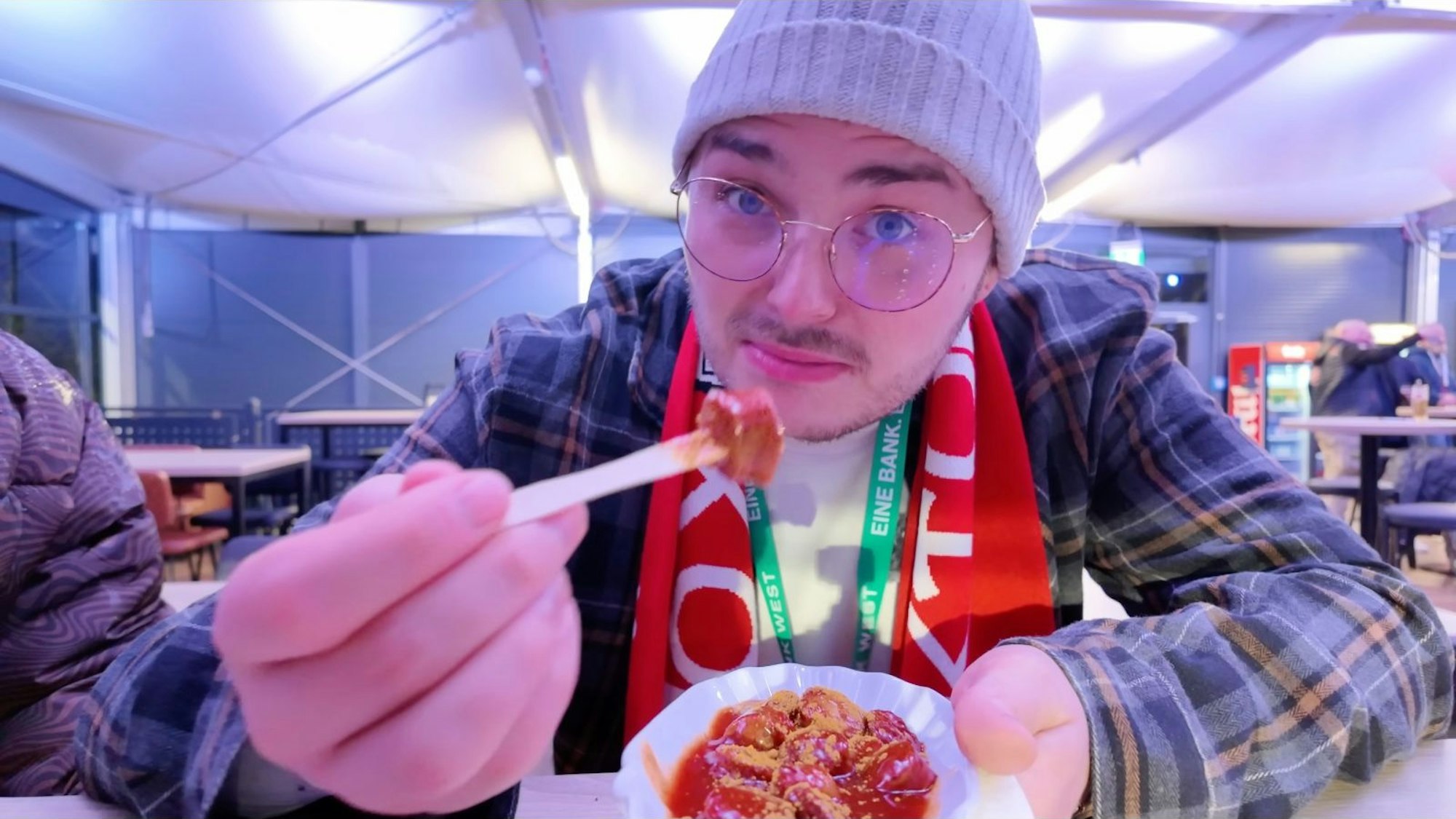 Der YouTuber Benji testet die Currywurst bei Viktoria Köln und guckt irritiert in die Kamera.