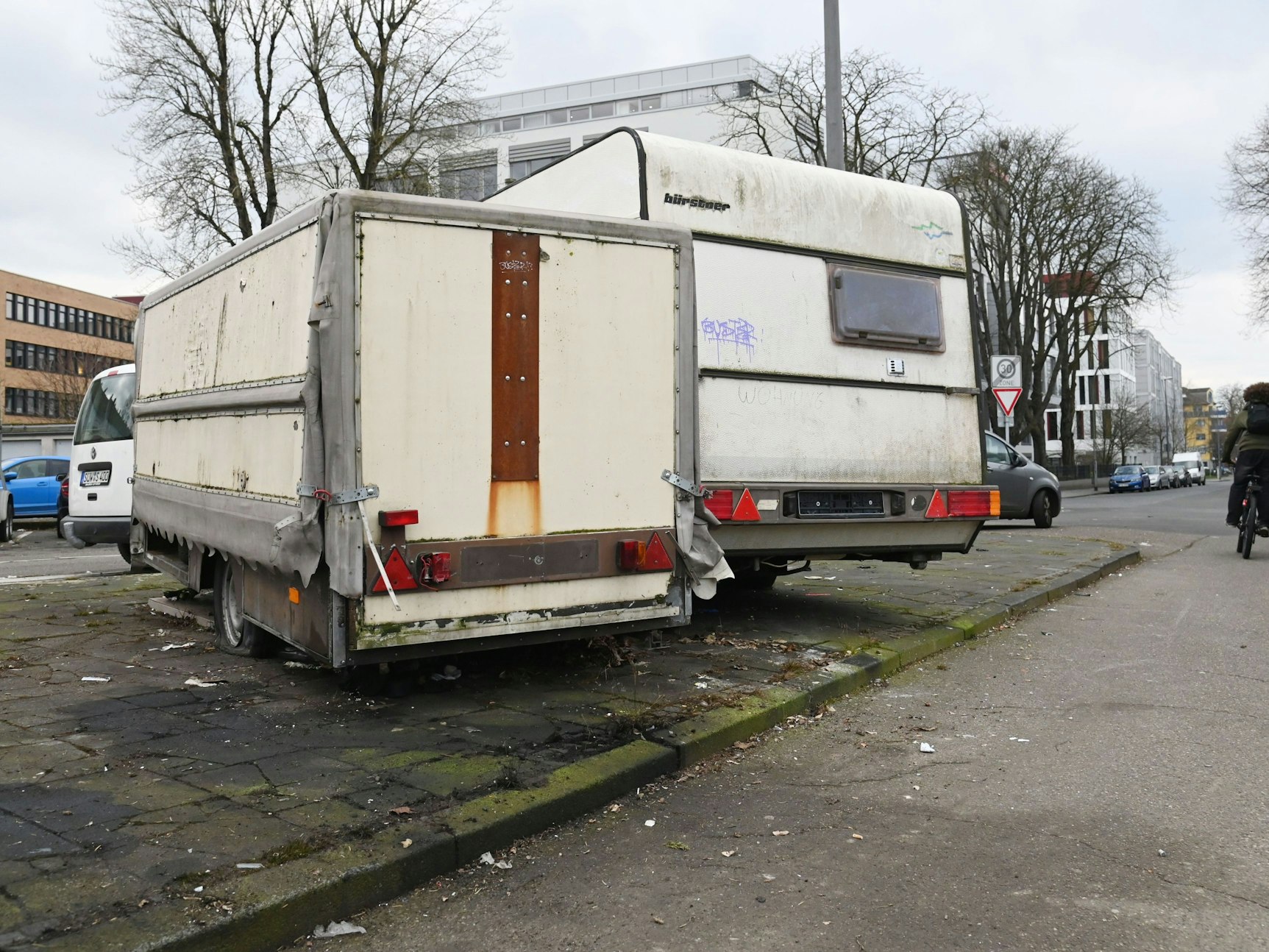 Ein Wohnmobil und ein alter Anhänger stehen verlassen auf einem Parkplatz in Köln.