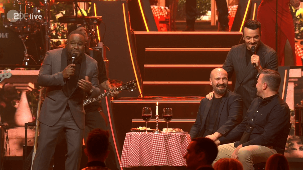 Starkoch Nelson Müller (l.) sang in der „Giovanni Zarrella Show“ am 15. Februar 2025 in Friedrichshafen gemeinsam mit dem Moderator für das künftige Ehepaar Pino und Stefan (v.l.).