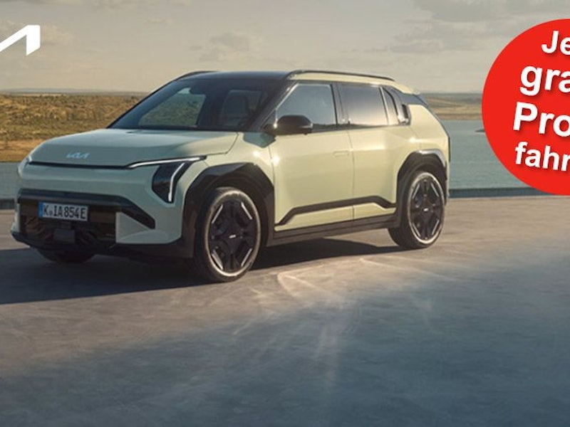 Ein Kia EV3 GT-line steht auf einer Betonfläche vor einem See und einer grünen Hügellandschaft.