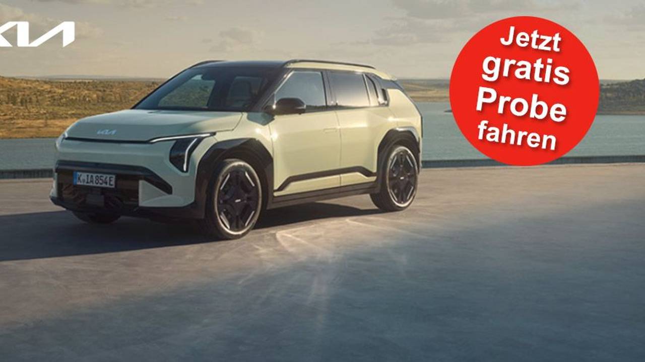 Ein Kia EV3 GT-line steht auf einer Betonfläche vor einem See und einer grünen Hügellandschaft.