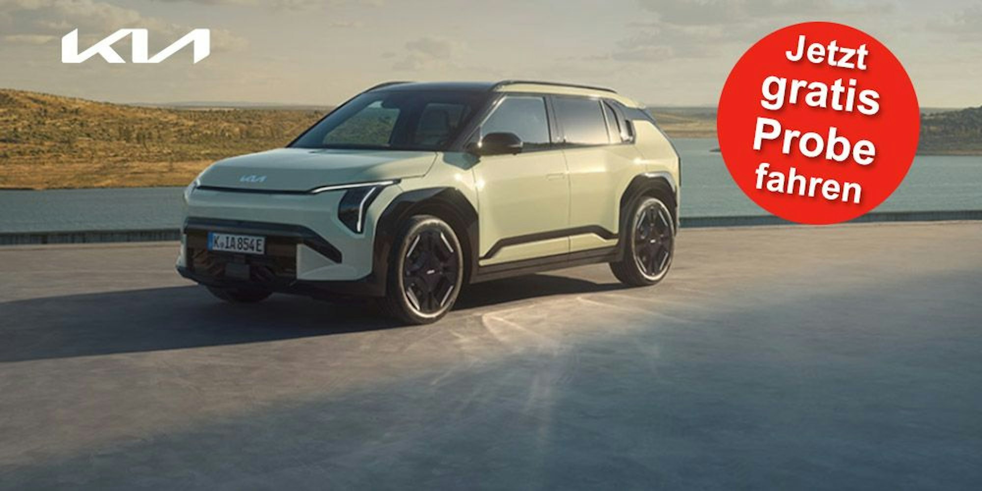 Ein Kia EV3 GT-line steht auf einer Betonfläche vor einem See und einer grünen Hügellandschaft.