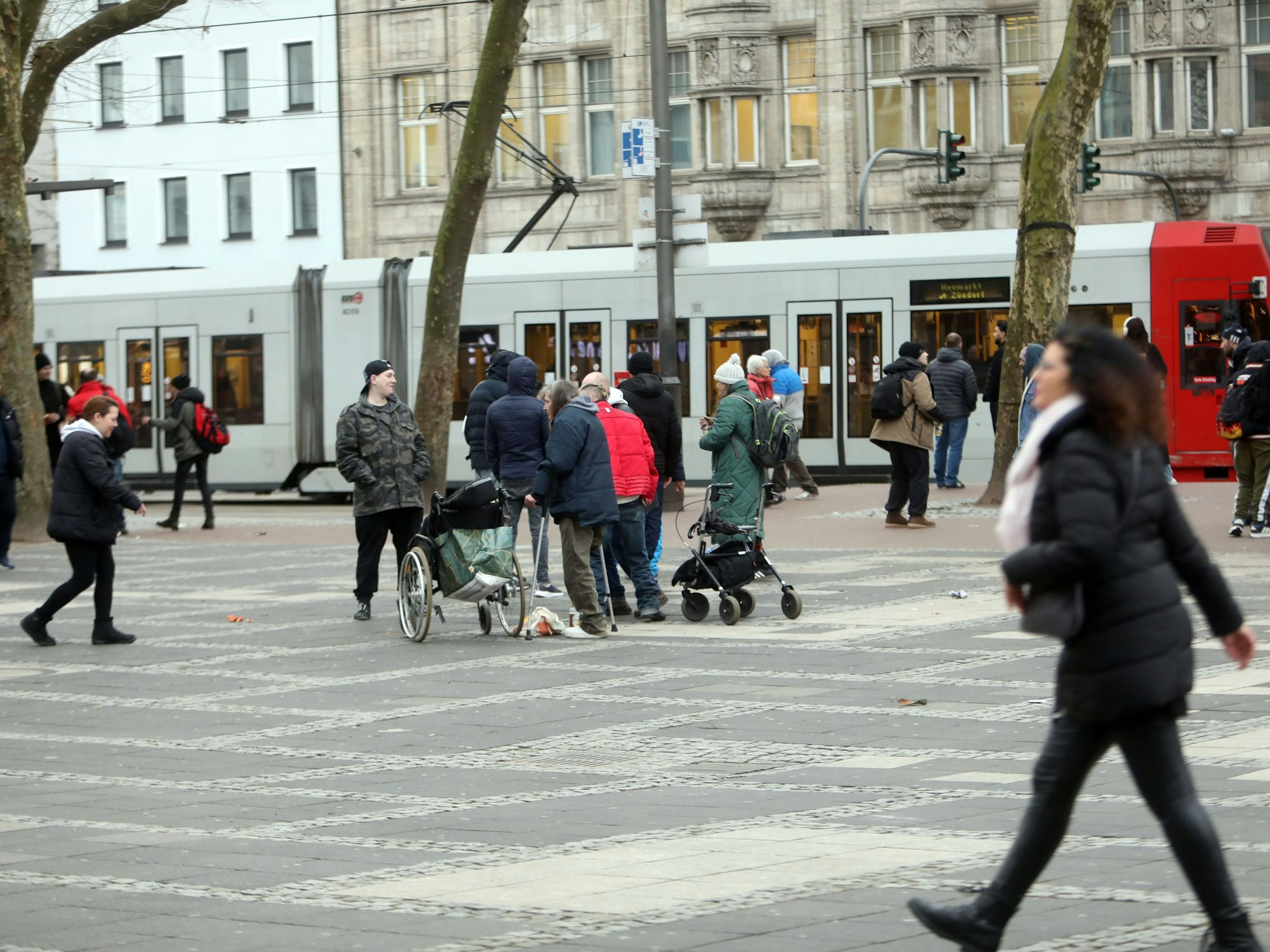 Menschen sind auf einem Platz unterwegs, eine Bahn hält.
