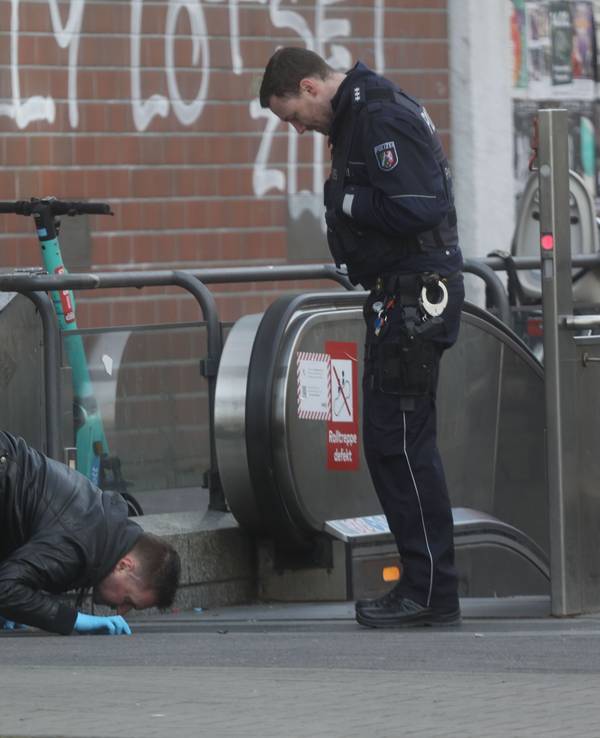 Ein Polizist kniet und fixiert etwas auf dem Boden, sein Kollege steht daneben.