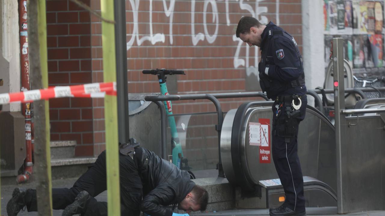 Ein Polizist kniet und fixiert etwas auf dem Boden, sein Kollege steht daneben.