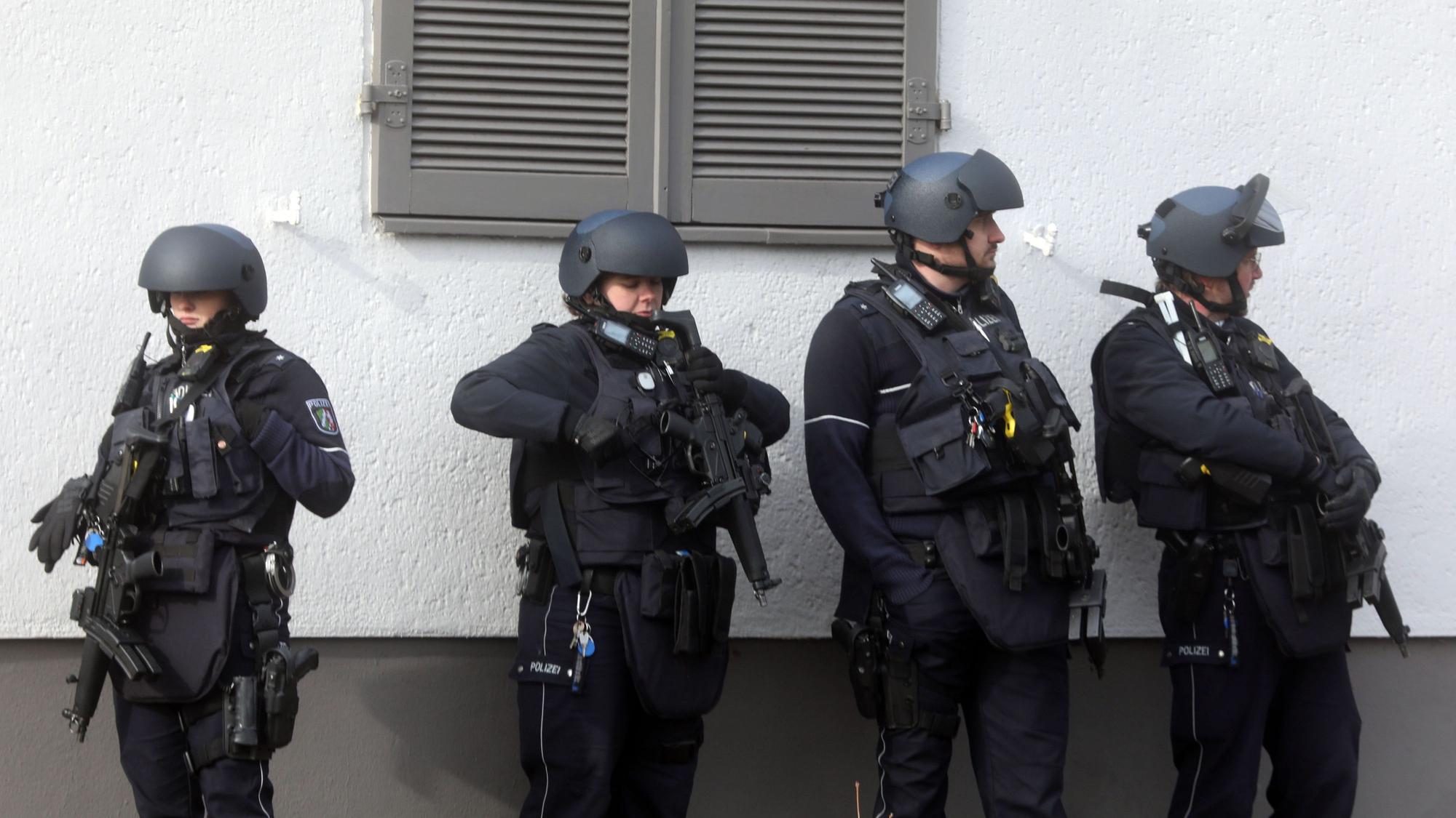 Vier Spezialkräfte stehen mit Maschinenpistolen vor einer Hauswand.