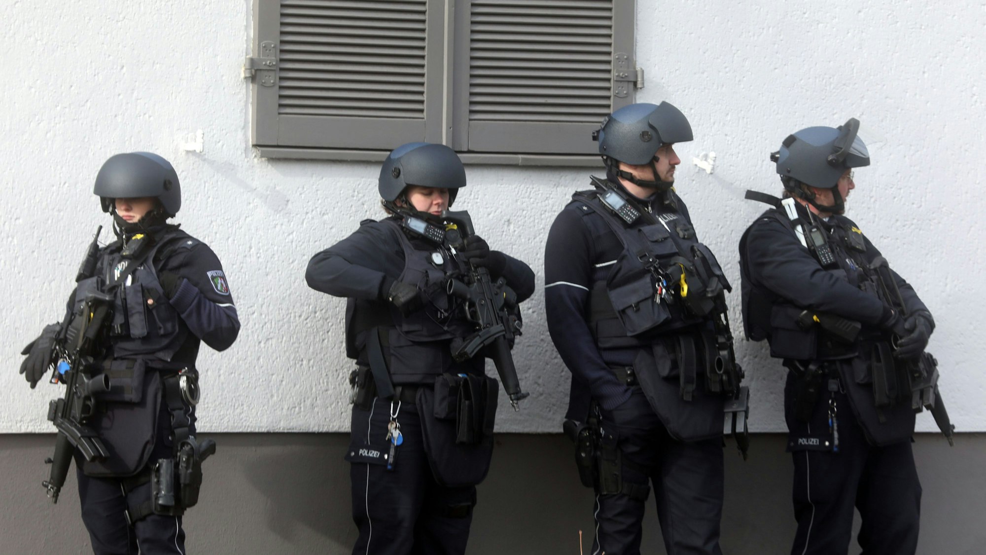 Vier Spezialkräfte stehen mit Maschinenpistolen vor einer Hauswand.