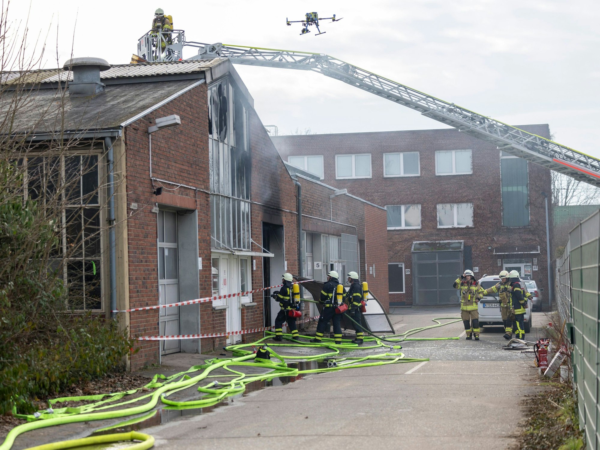 Feuerwehrleute stehen vor einer Halle, eine Drehleiter reicht auf das Dach.