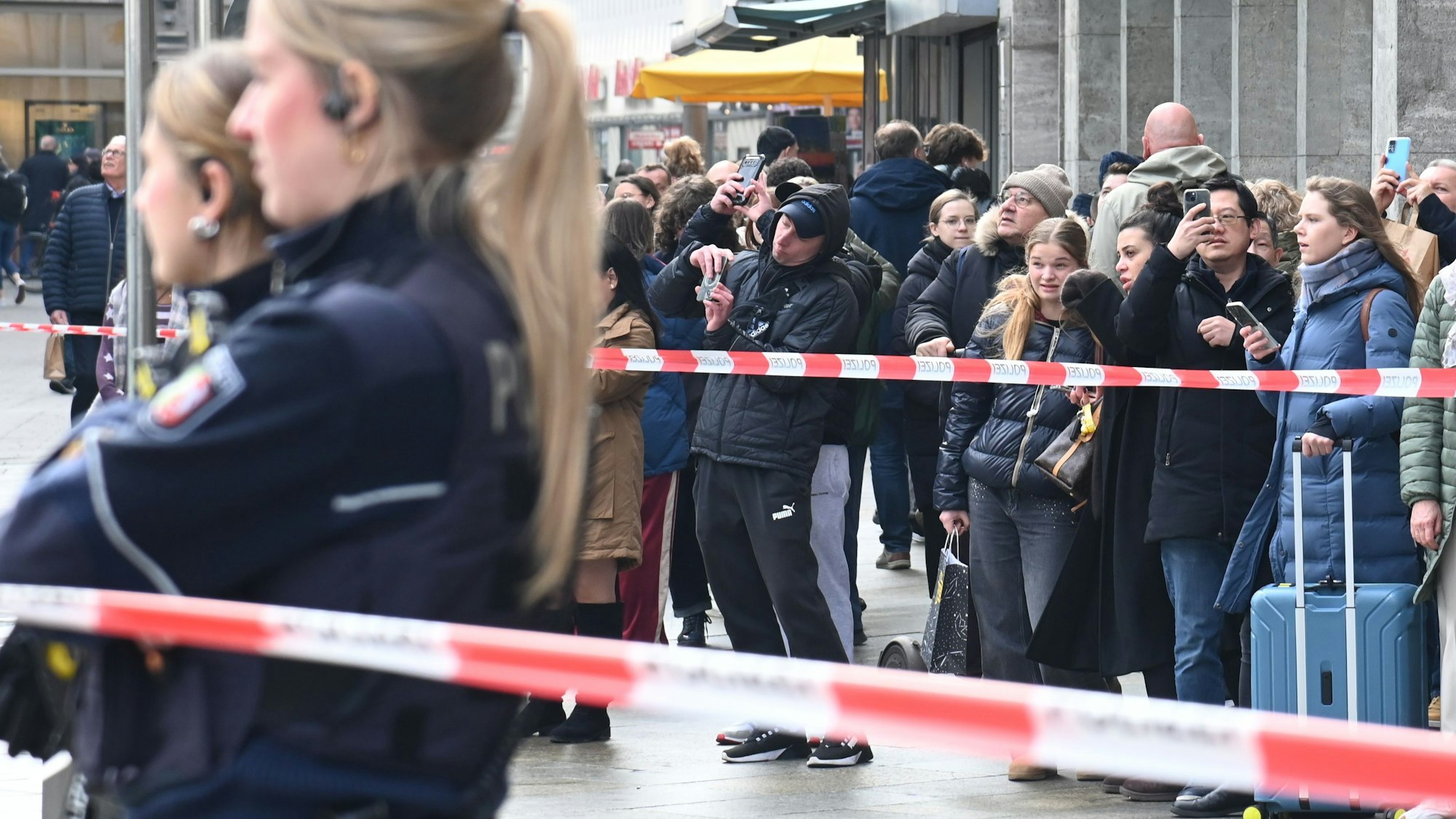 Schaulustige stehen an der Polizeiabsperrung und machen Fotos.