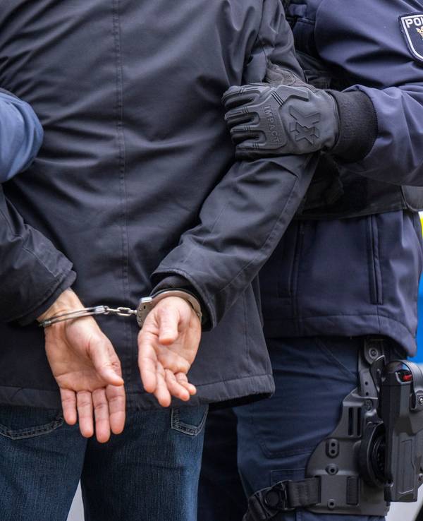 Die Polizei führt eine Person ab, deren Hände auf dem Rücken gefesselt sind.