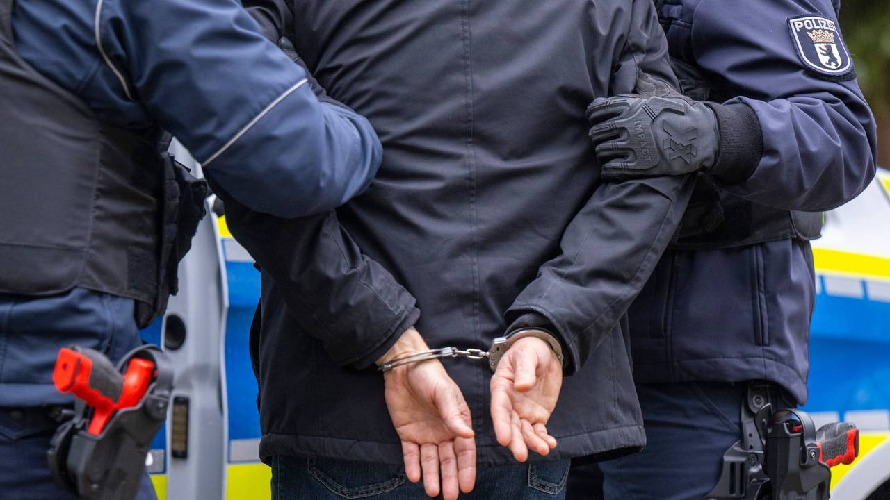 Die Polizei führt eine Person ab, deren Hände auf dem Rücken gefesselt sind.