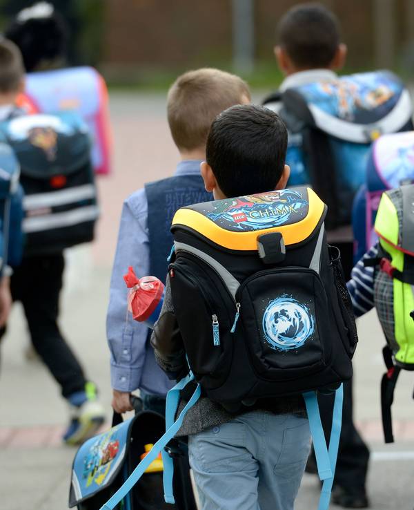 Kinder gehen mit ihren Ranzen zu Schule.