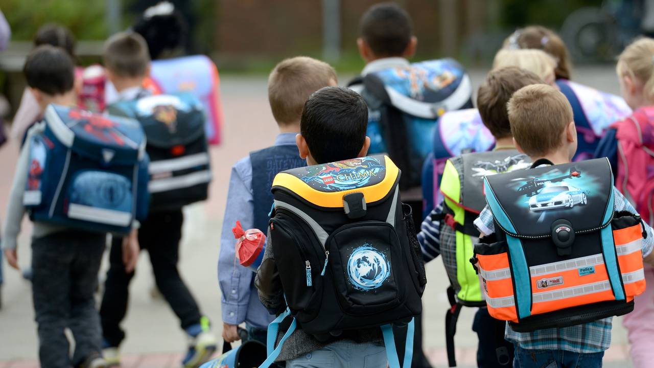 Kinder gehen mit ihren Ranzen zu Schule.