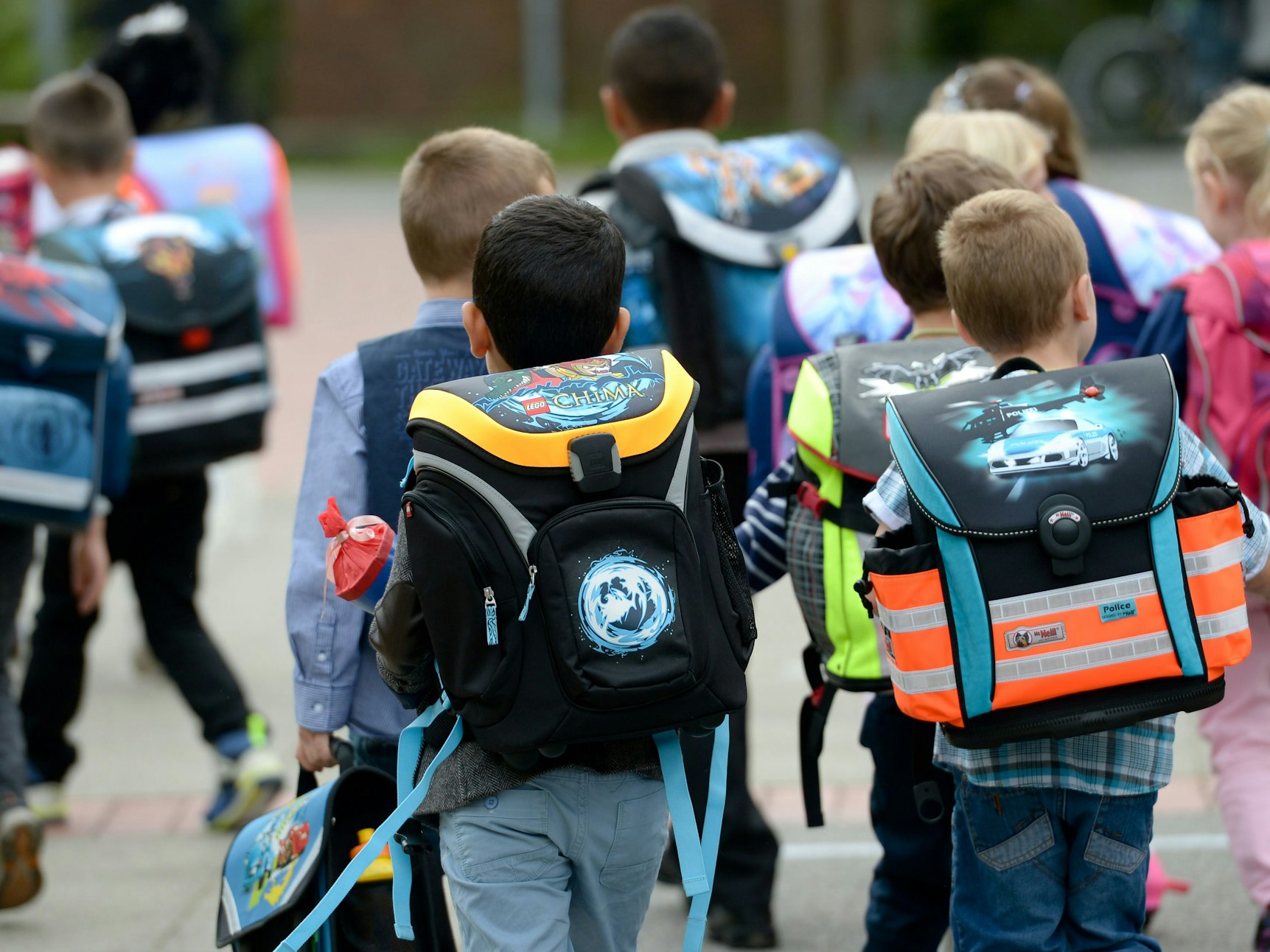 Kinder gehen mit ihren Ranzen zu Schule.